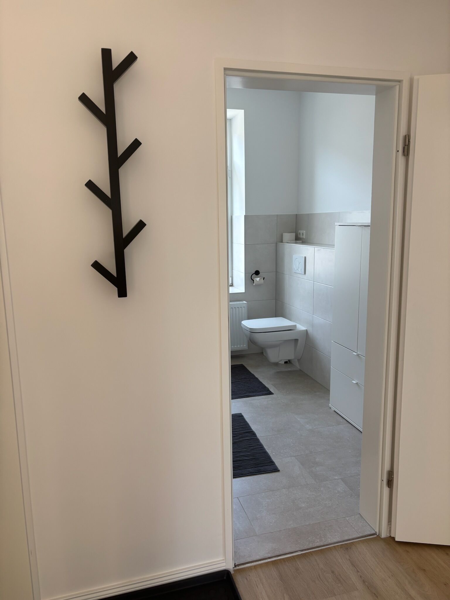 Um corredor que dá para um banheiro com vaso sanitário, radiador e armários.