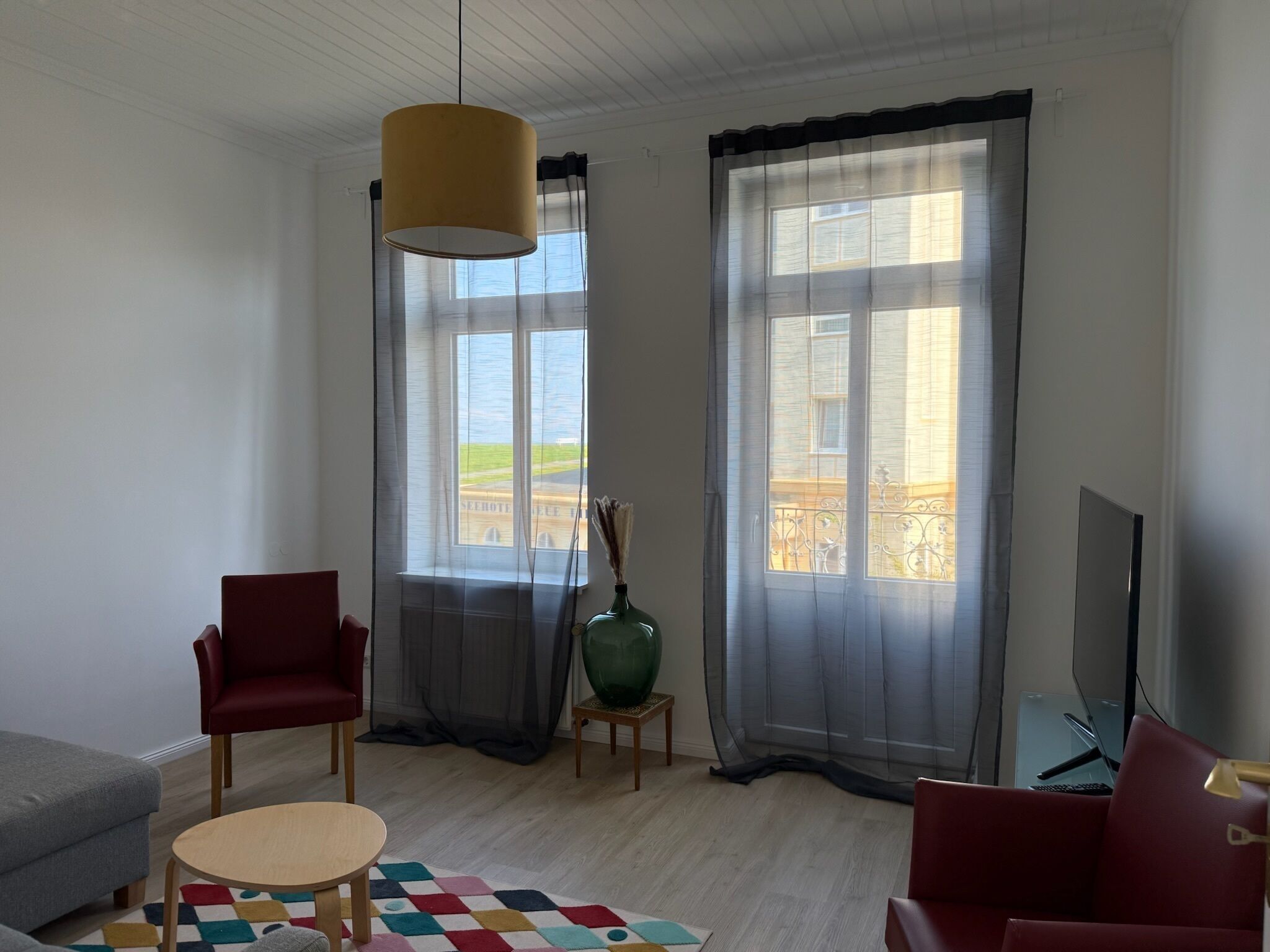 A modern living room with a sofa, armchairs, a coffee table, a TV, and a large window with curtains.