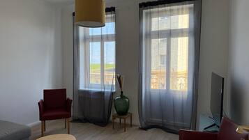 Uma sala de estar moderna com sofá, poltronas, mesa de centro, televisão e uma janela grande com cortinas.