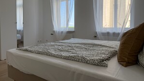 Une chambre à coucher avec un lit, une armoire et deux fenêtres ornées de rideaux légers.