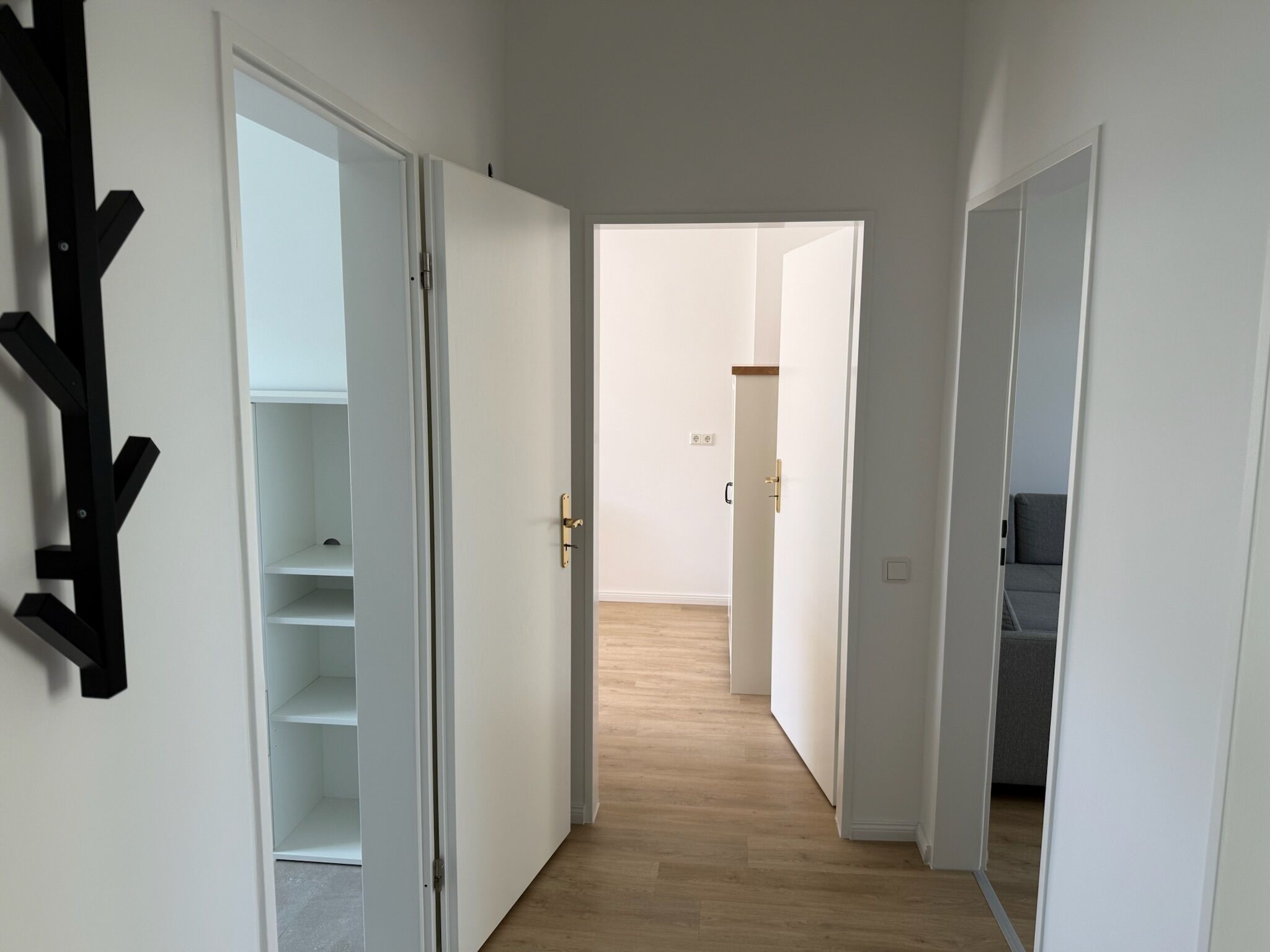 A hallway with open doors leading to a room with a grey sofa and a wooden floor.
