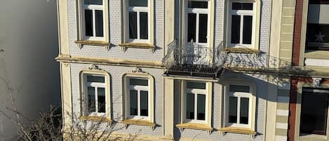 A multi-story building with a symmetrical facade, featuring evenly spaced windows with decorative moldings and a central balcony with ornate iron railings.