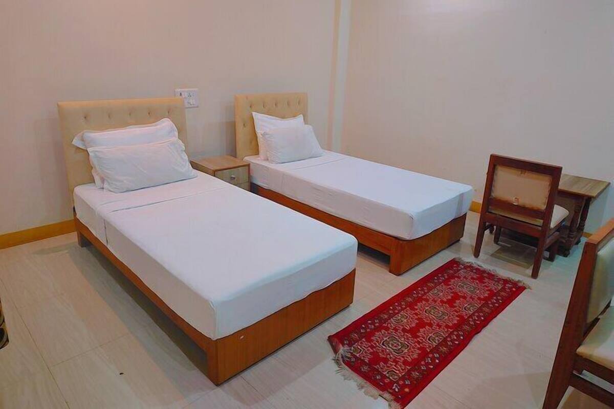 A room with two single beds, a wooden nightstand, a chair, and a red patterned rug.