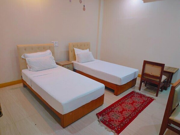 Una habitación con dos camas individuales, una mesita de noche de madera, una silla y una alfombra roja estampada.