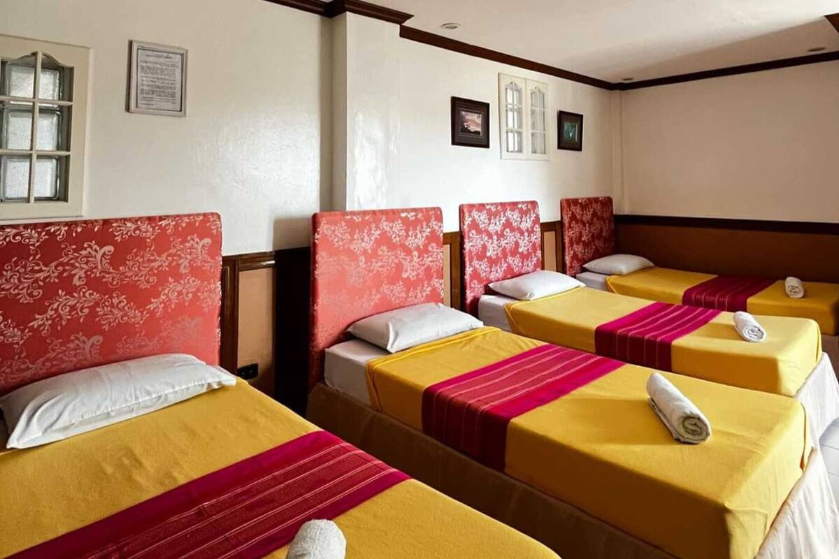 A hotel room with four beds, each with yellow bedding and red headboards.