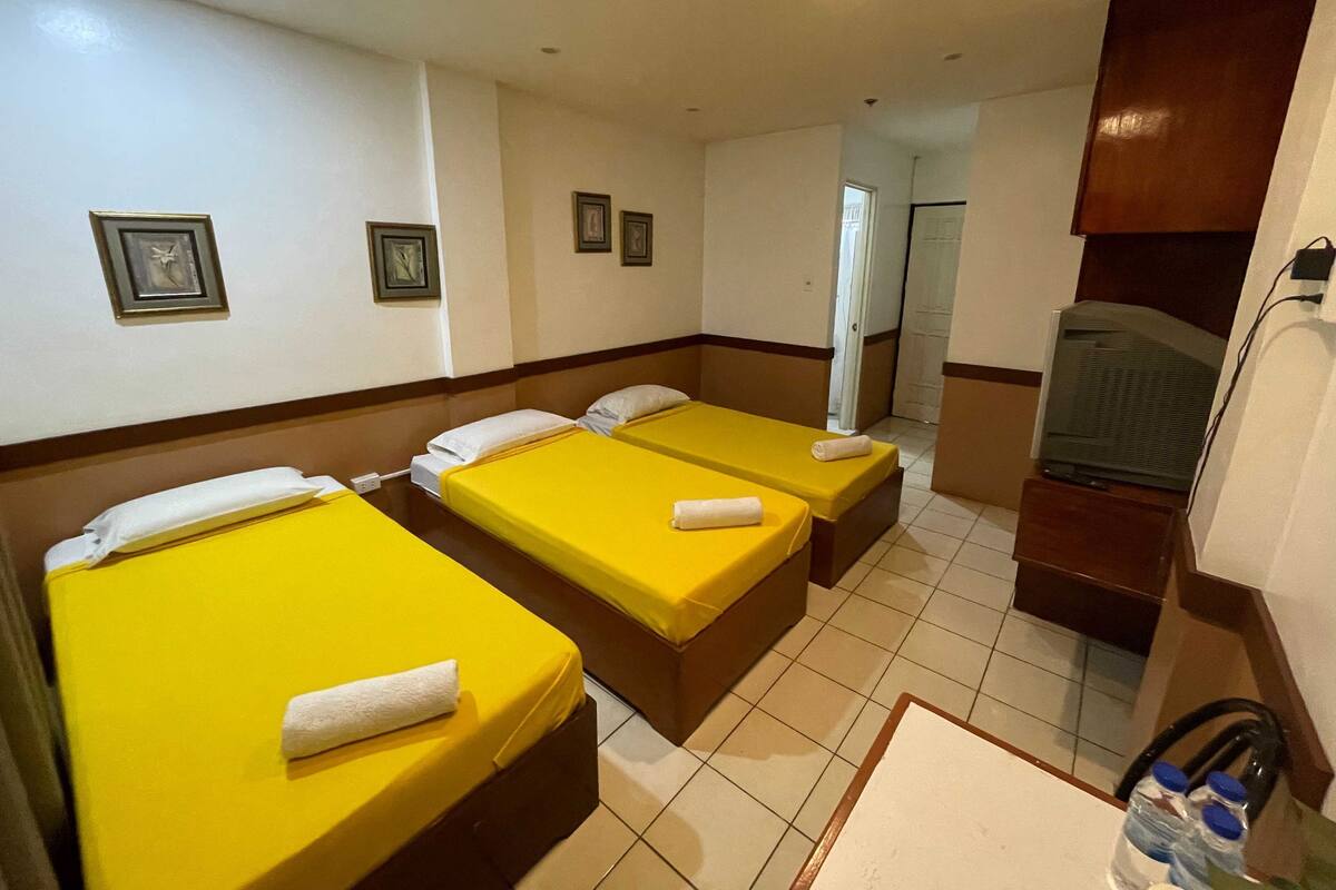 A hotel room with two single beds, a television, a small table, and a bathroom visible through an open door.