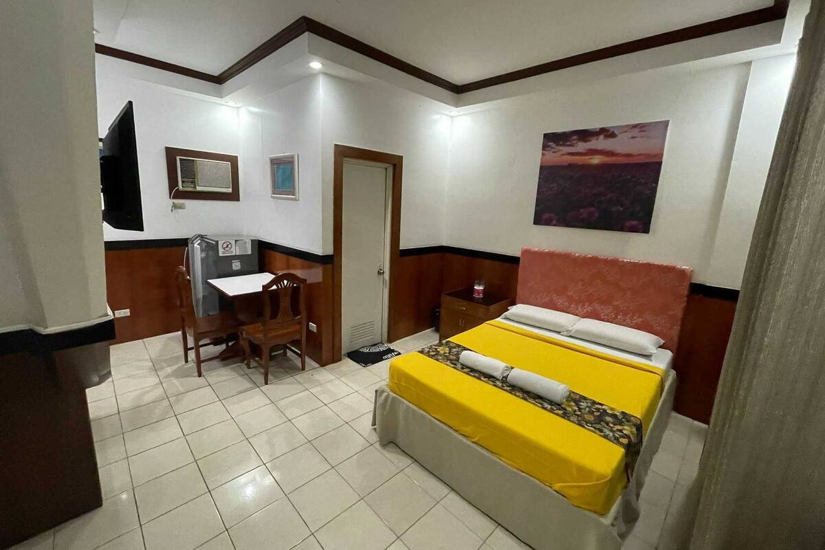 A hotel room with a bed, a desk, a chair, and a door.