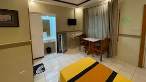 A hotel room with a bed, a desk, a chair, a TV, and a refrigerator. - Palette Gems Hotel and Conference Center (Antipolo)