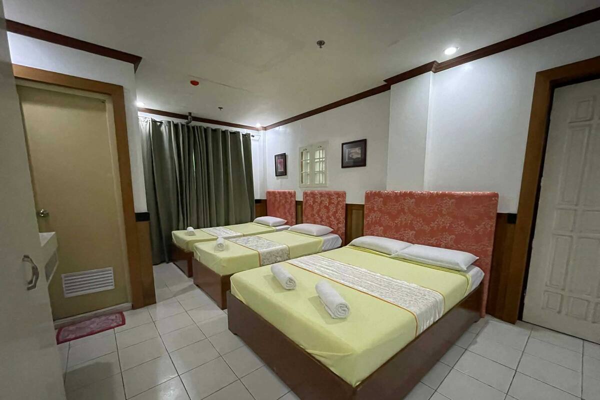 A hotel room with three beds, each with a neatly made bedspread and towels.