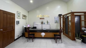 A reception desk with a sign reading "GEMS HOTEL" and a clock above it. There are two wooden chairs in front of the desk, a potted plant, and a small statue on the counter. - Palette Gems Hotel and Conference Center (Antipolo)