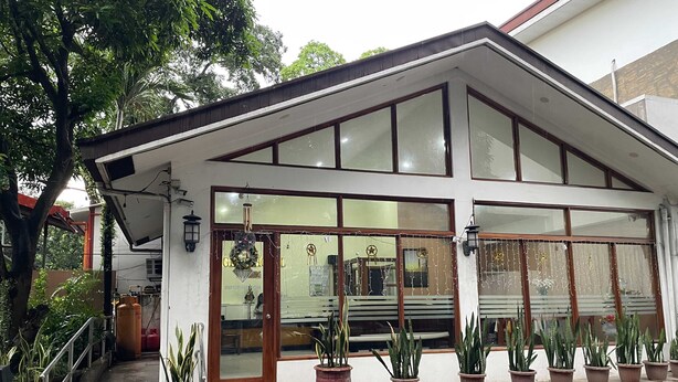 A modern building with a sloped roof, large glass windows, and a front entrance with a wooden door. There are potted plants along the front steps. - Palette Gems Hotel and Conference Center (Antipolo)