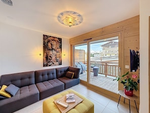 A modern living room with a large sofa, a coffee table with a book and a phone, and a painting of a lion. - Le Fraké-appartement-2pers-proche piste (Les Gets)