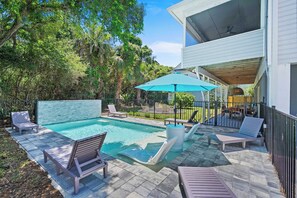 Piscina com espreguiçadeiras, varanda coberta e vista para uma casa.