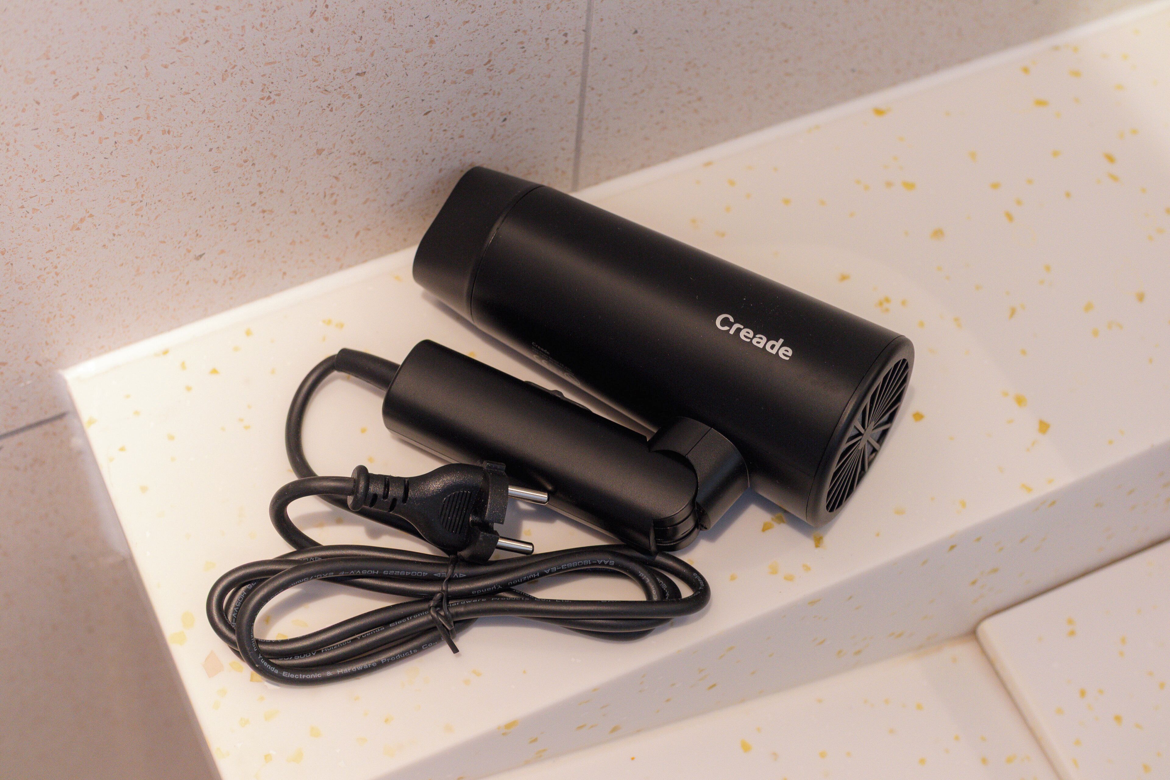 Un appareil électronique noir, doté d’un câble, est posé sur une surface blanche parsemée de taches jaunes.