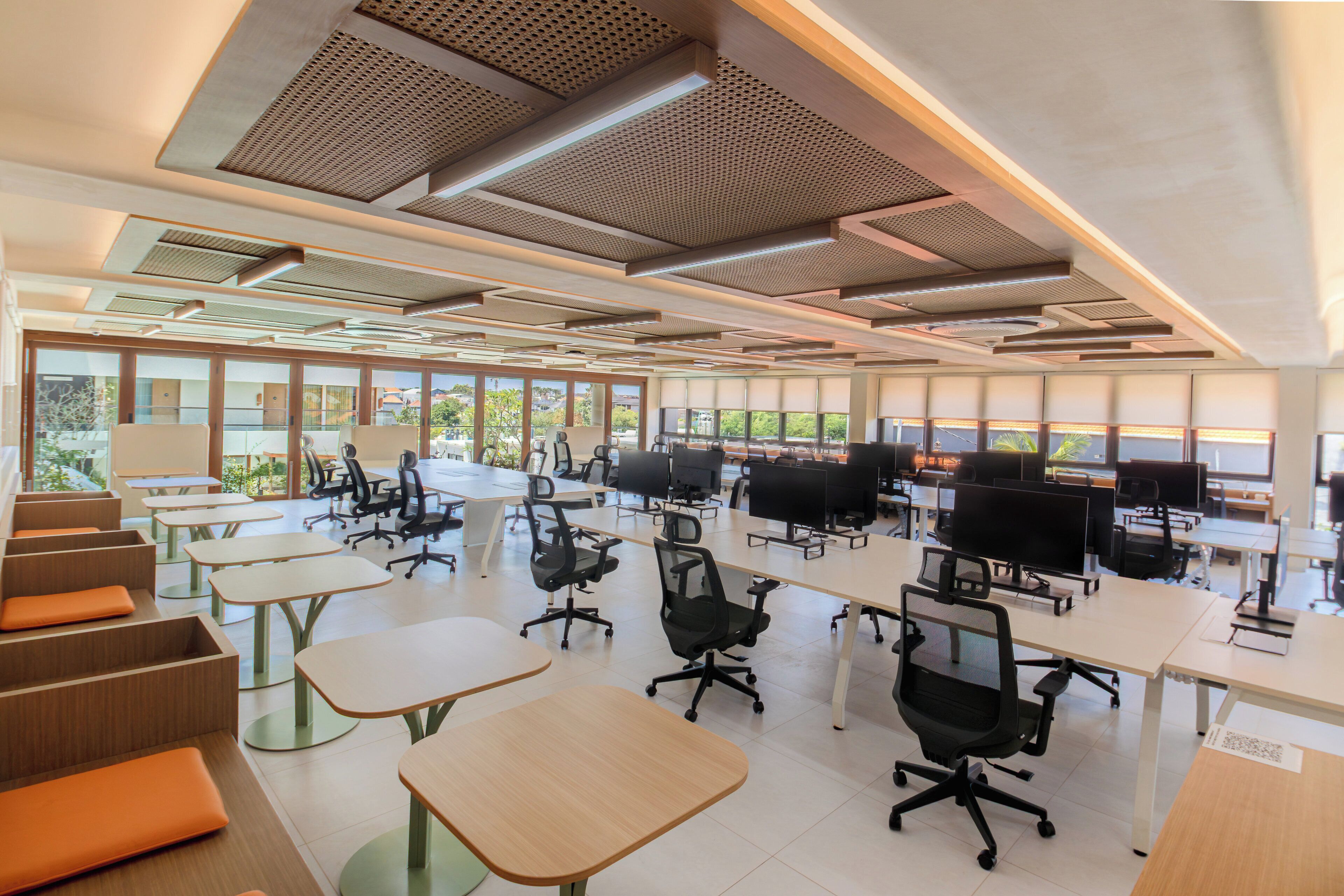 Un espacio de oficina moderno con varios puestos de trabajo, sillas ergonómicas y amplios ventanales que ofrecen luz natural.