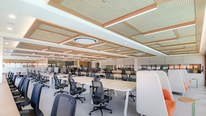 Et moderne kontormiljø med rækker af skriveborde og stole, et stort konferencemødebord og et loft med et unikt perforeret design.