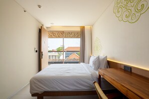 A hotel room with a bed, a wooden bench, a window with a view of buildings, and a decorative wall pattern.