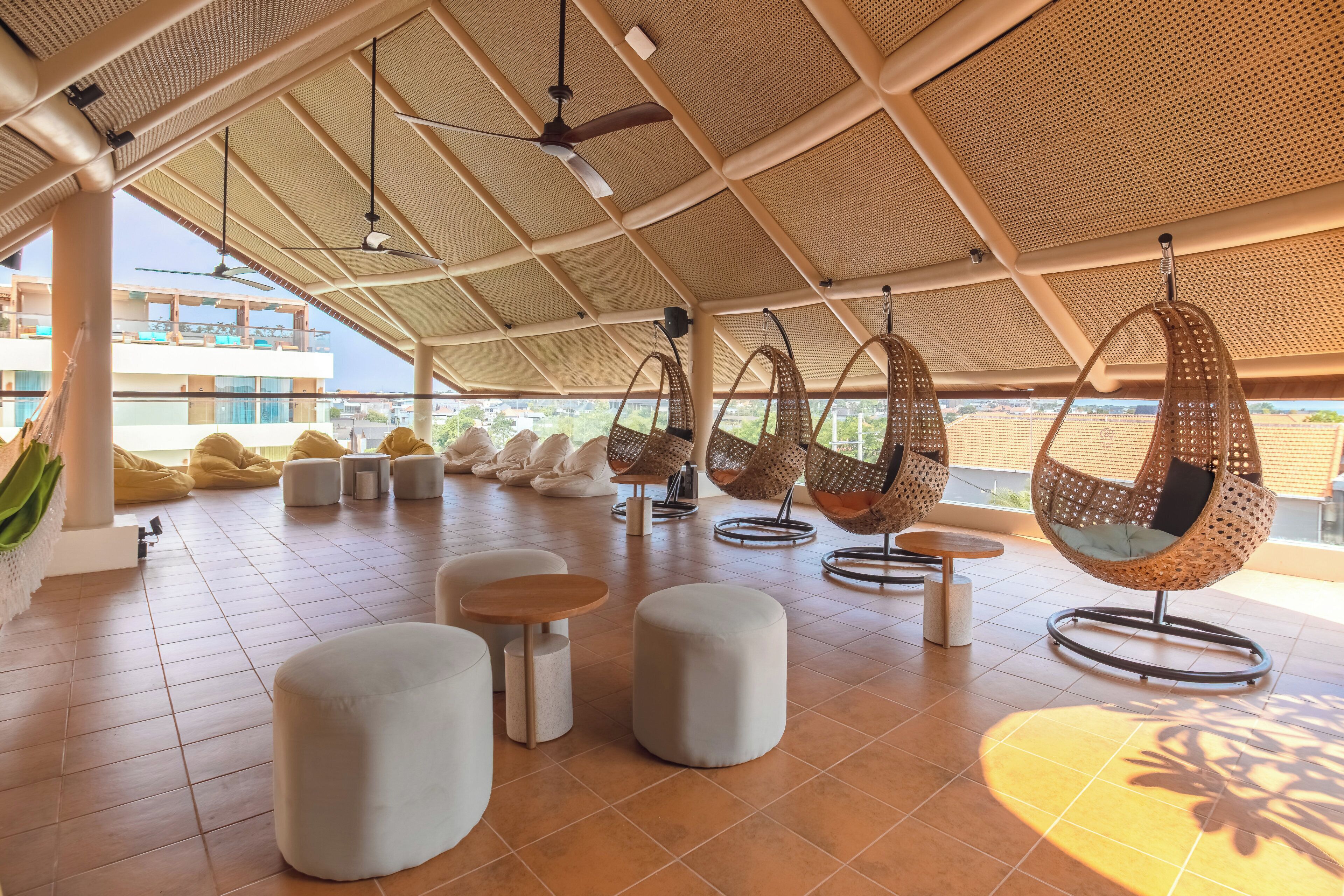 A modern outdoor seating area with hanging chairs, round tables, and cushioned seating.