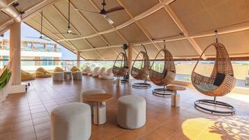 A modern outdoor seating area with hanging chairs, round tables, and cushioned seating.