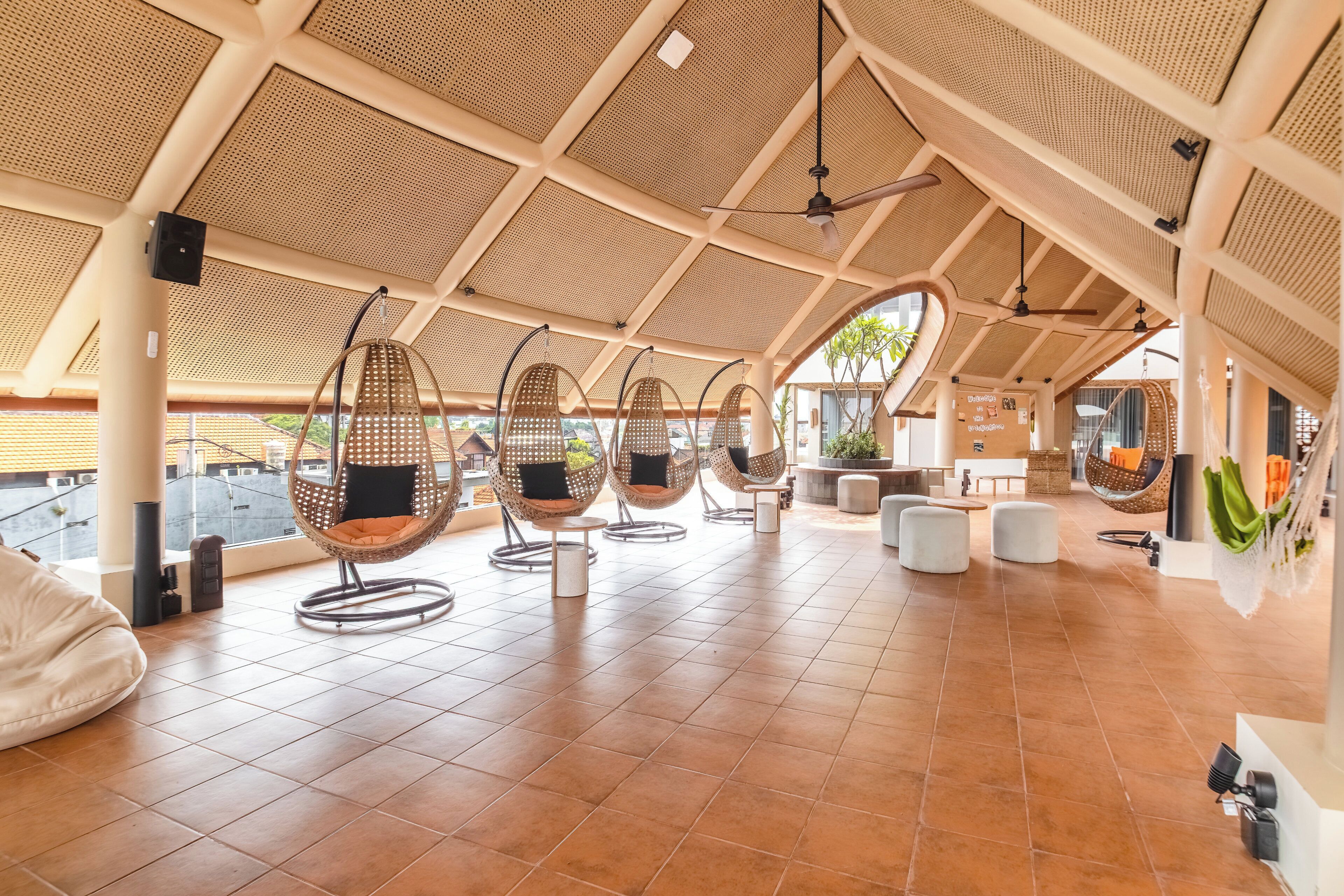 A spacious terrace with hanging chairs, a tiled floor, and a high ceiling with a woven pattern.
