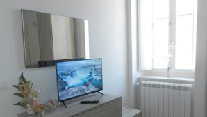 A bedroom with a wooden dresser, a flat-screen TV, a window with white blinds, and a radiator. - Design and History in the Heart of L'Aquila Capital of Culture 2026 (L'Aquila)