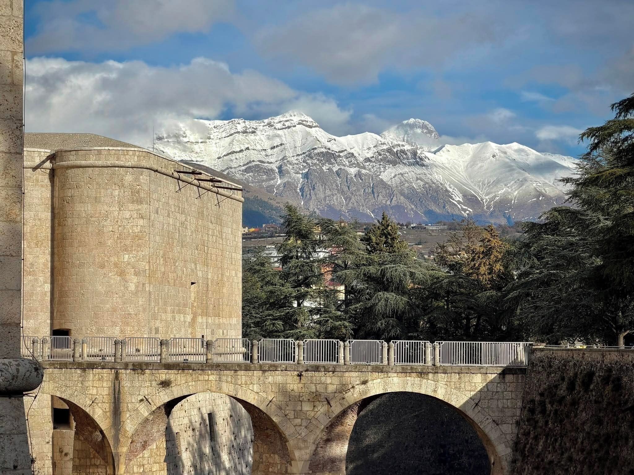 A stone bridge with arches, a cylindrical structure, and a mountainous backdrop.