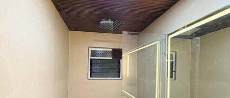 A small, modern bathroom with a wooden ceiling, a glass shower enclosure, a toilet, and a vanity with a mirror.