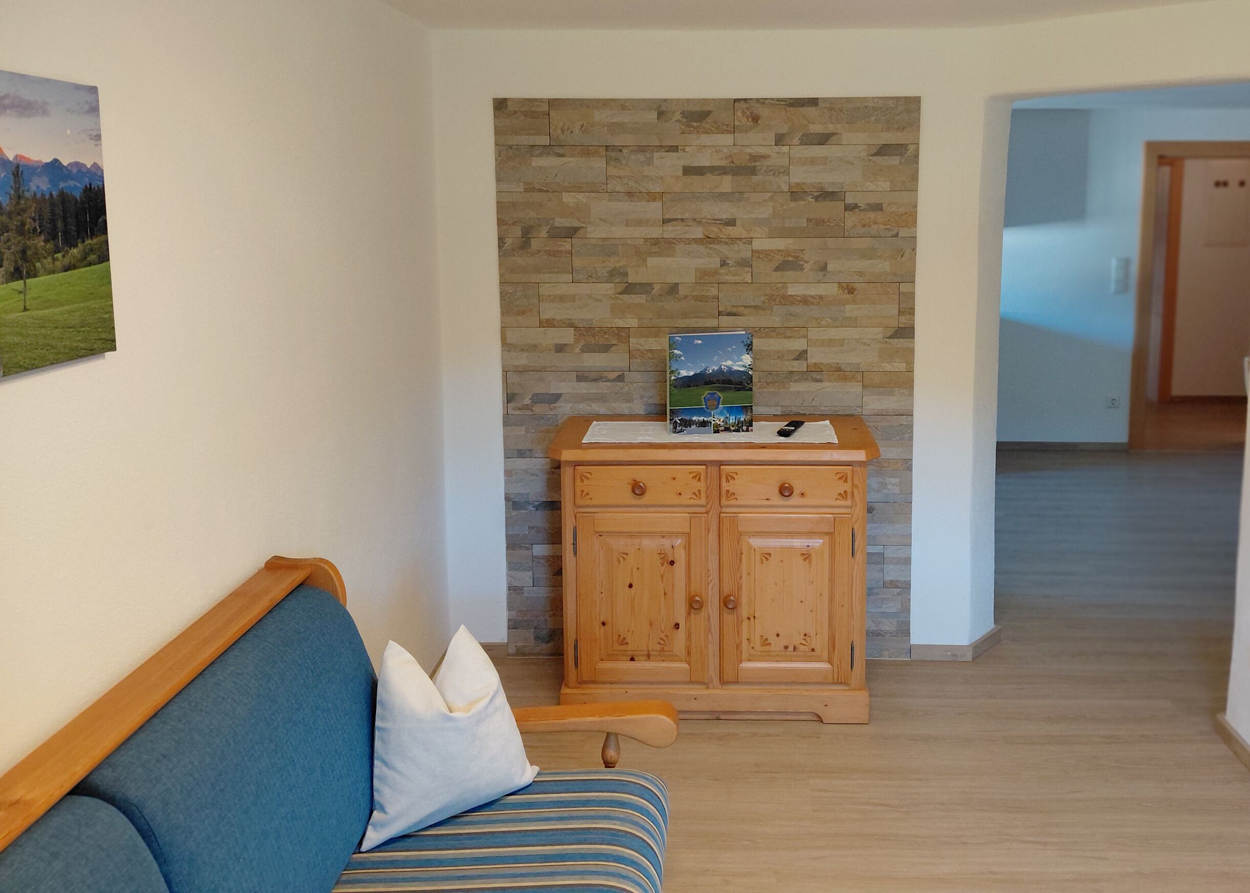 Une pièce avec un meuble en bois, un tableau encadré au mur et un canapé bleu avec des coussins.