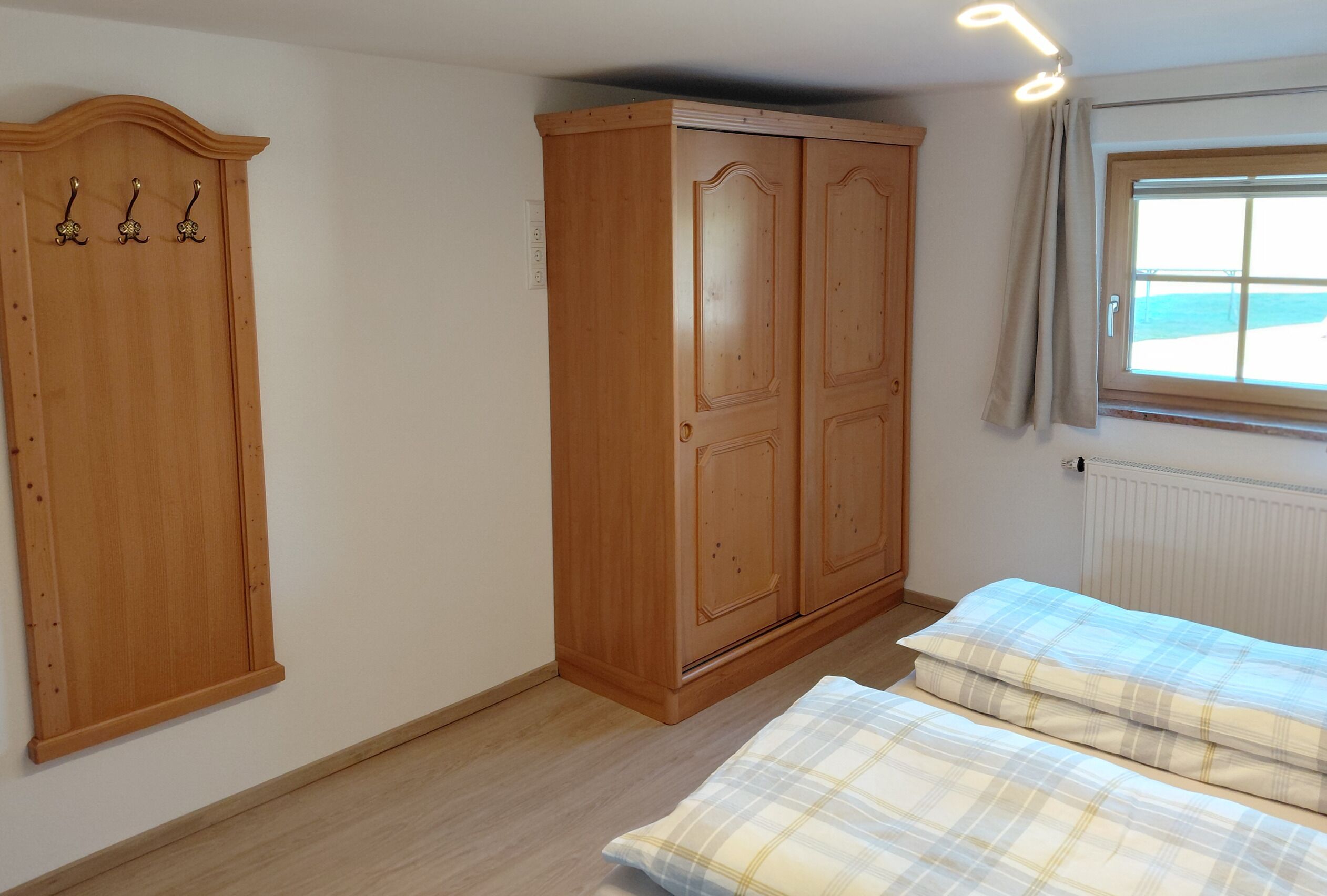 A bedroom with a bed, a wooden wardrobe, and a window with curtains.