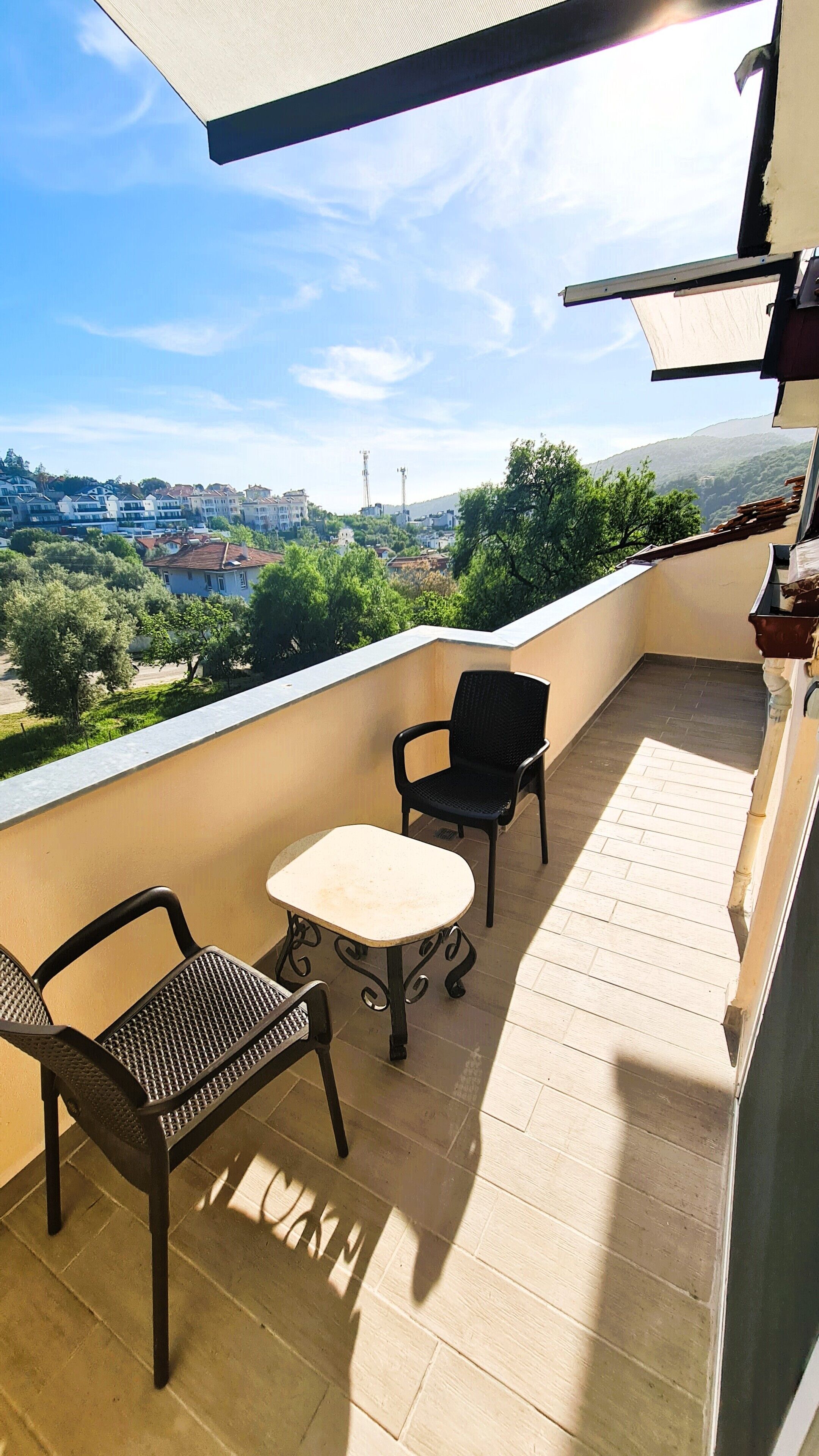 En balkon med to stole og et lille bord, med udsigt over et boligområde med huse og grønt.