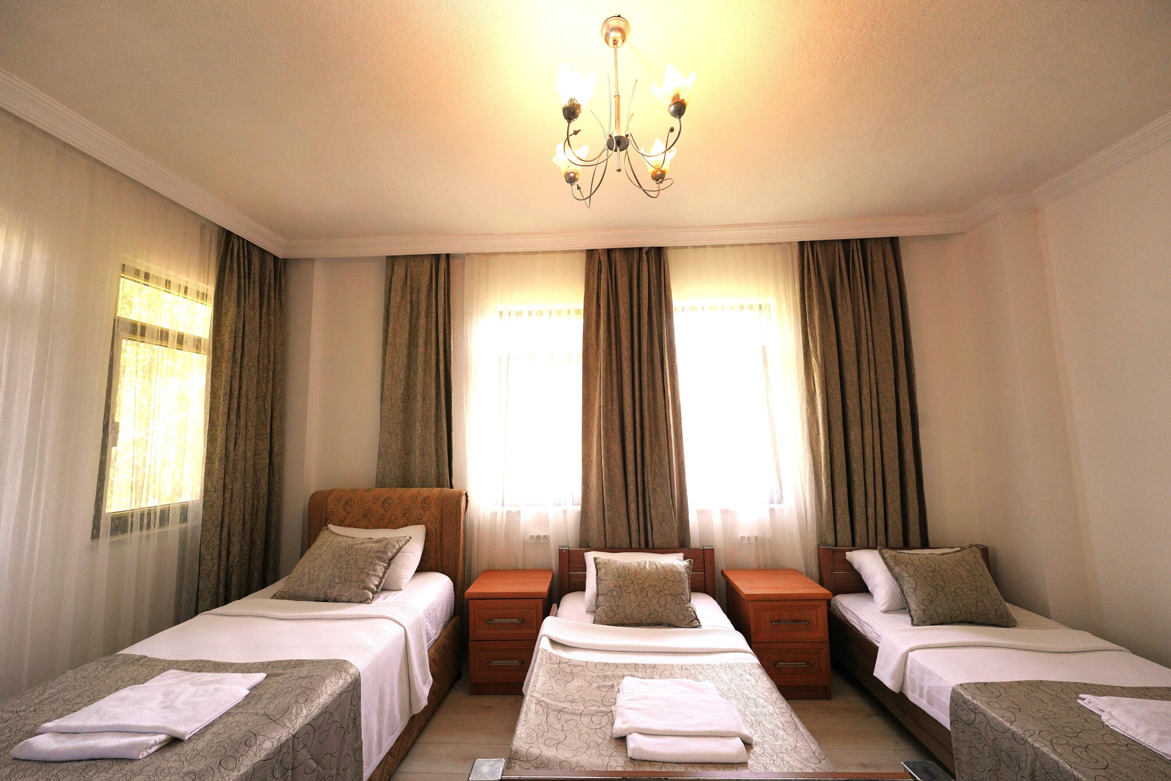 Une chambre d’hôtel avec trois lits simples, un lustre et des rideaux aux fenêtres.