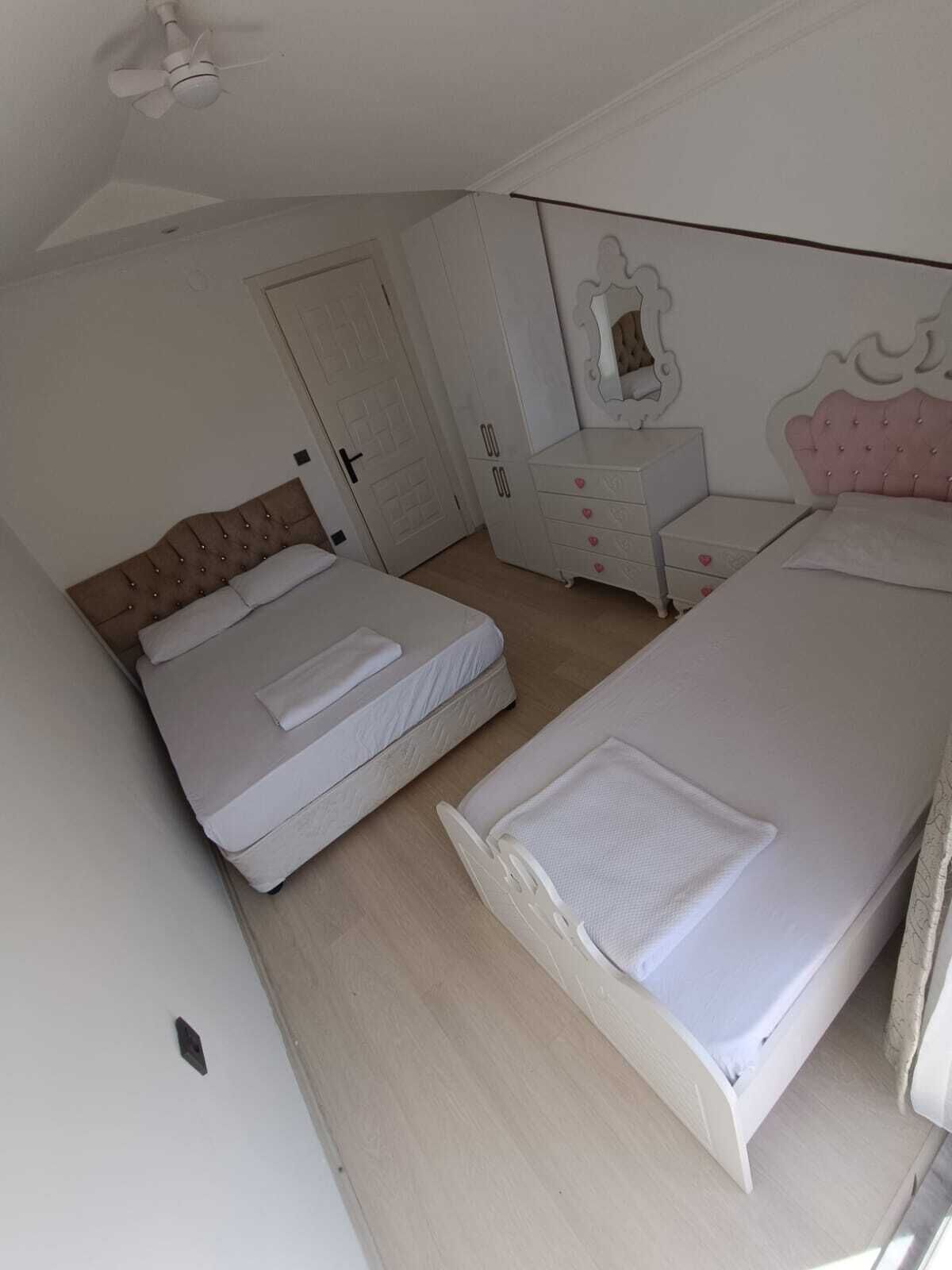Una camera da letto con due letti, una cassettiera, un comodino, una ventola a soffitto e una porta.