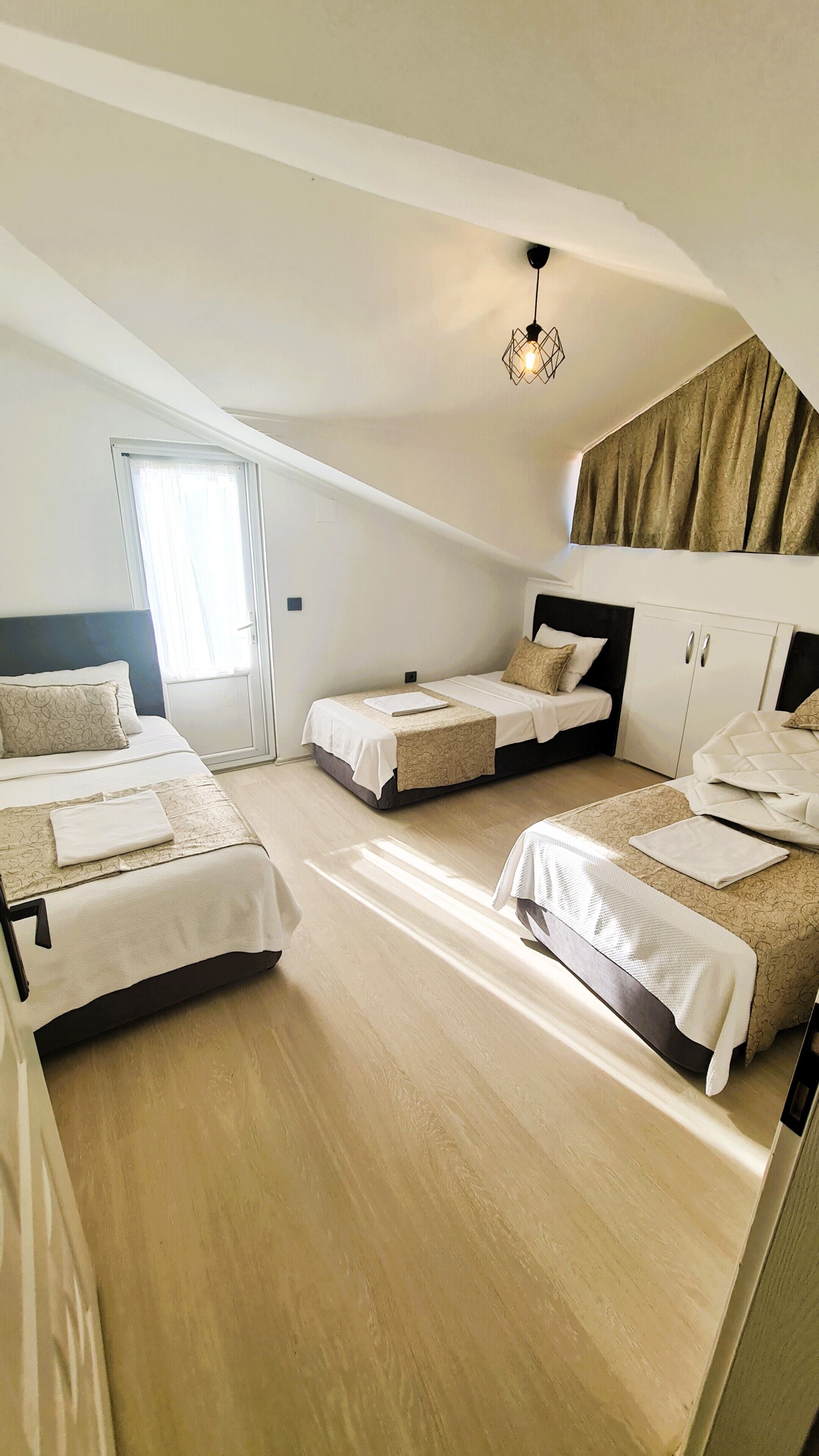 A spacious attic bedroom with three beds, a sloped ceiling, and a large window.