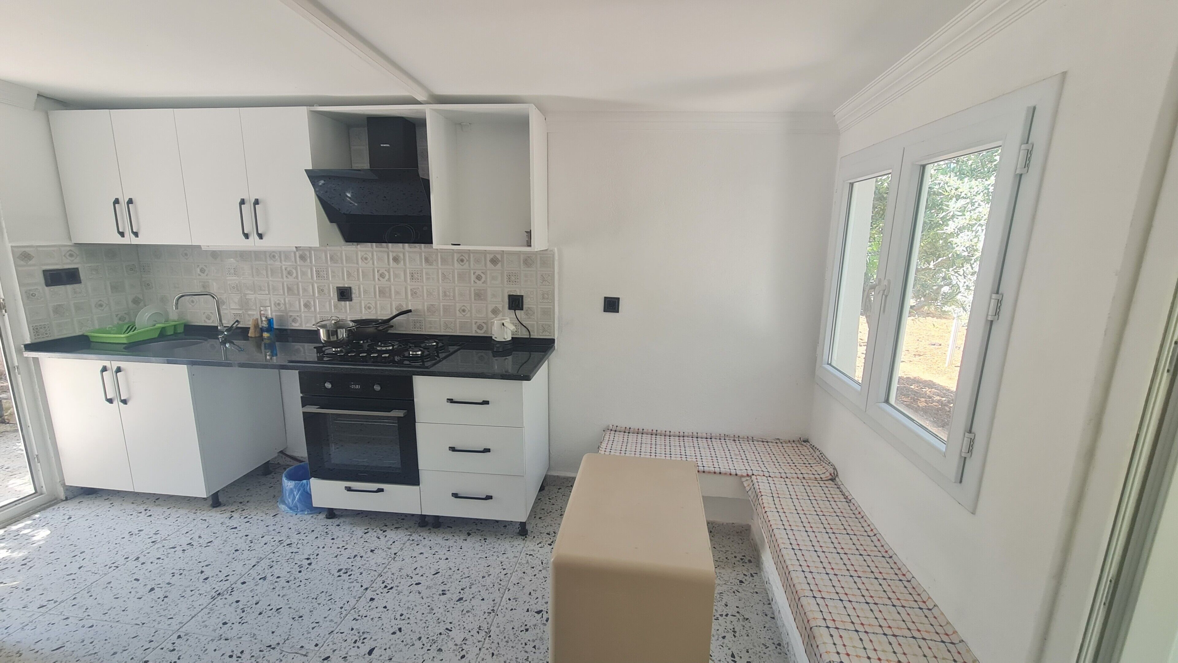 Une cuisine avec des armoires blanches, un comptoir noir, une cuisinière et une fenêtre.