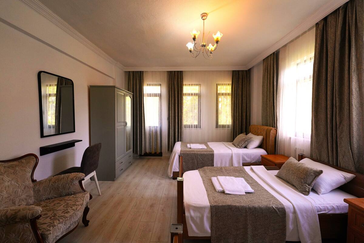 A hotel room with two beds, a sitting area with a sofa, a mirror, and a chandelier.