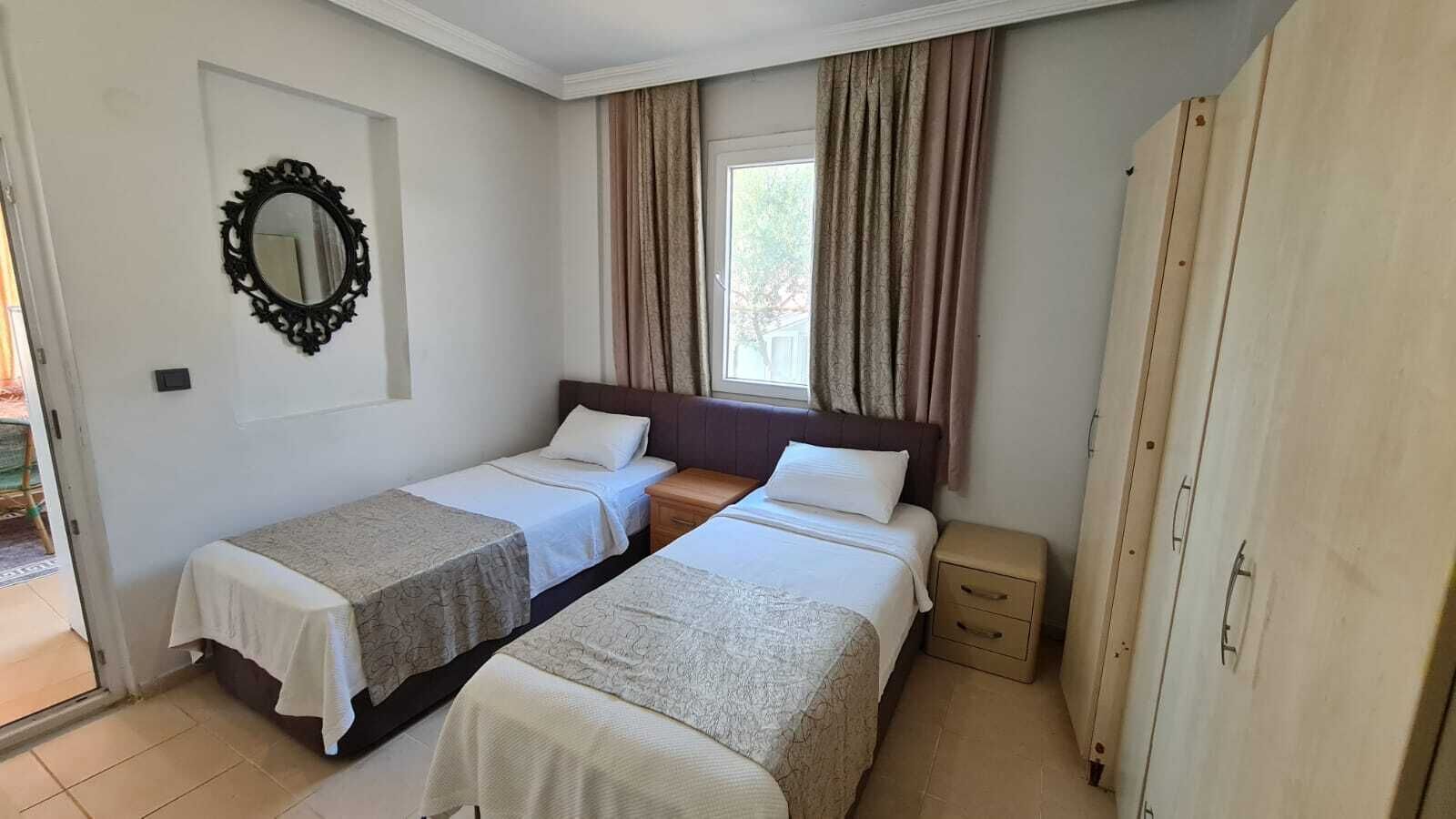 A room with two beds, a mirror, a window with curtains, and a wooden wardrobe.