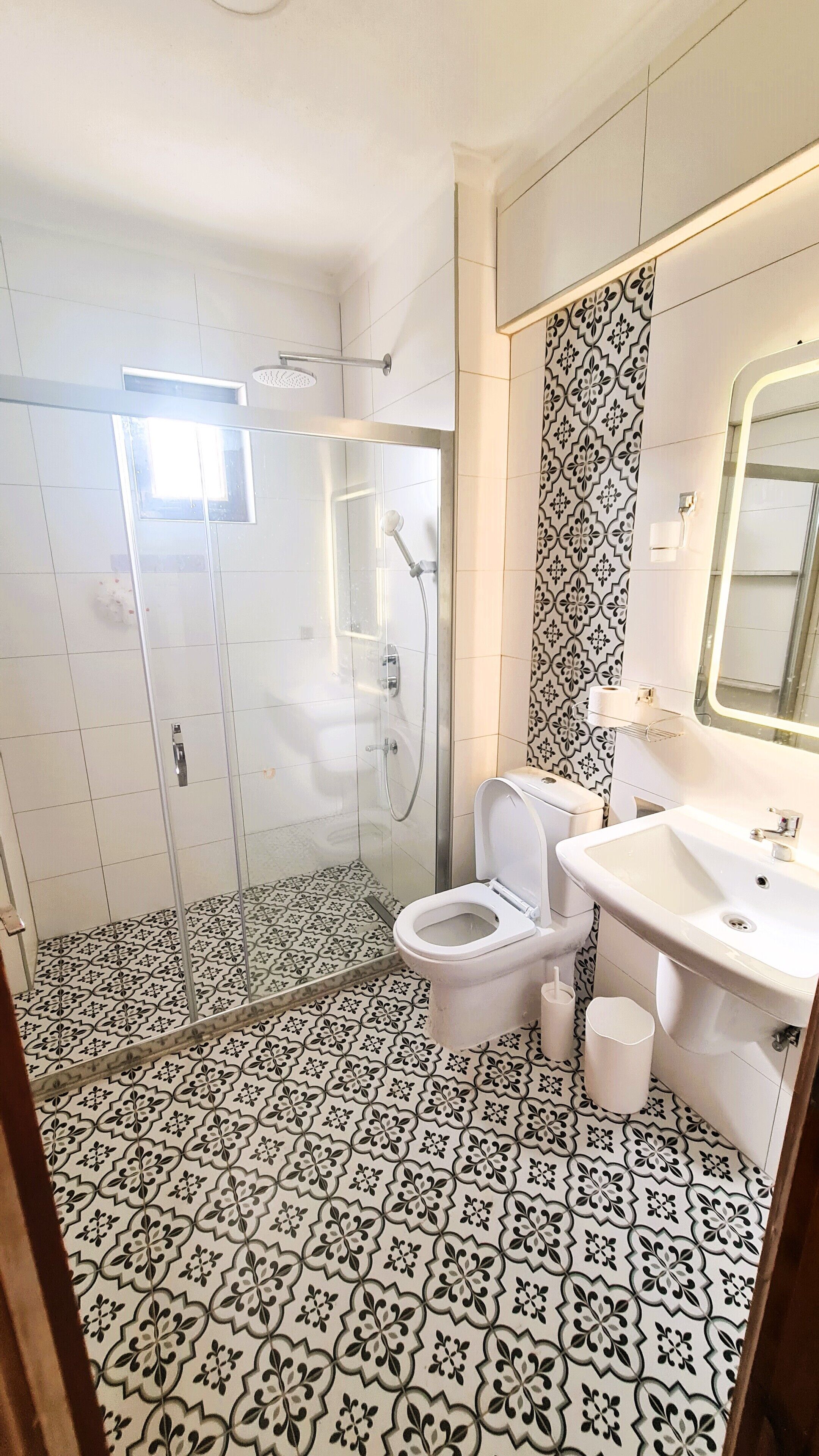 A bathroom with a shower, toilet, and sink, featuring patterned tiles and a mirror.