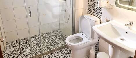 A bathroom with a shower, toilet, and sink, featuring patterned tiles and a mirror.