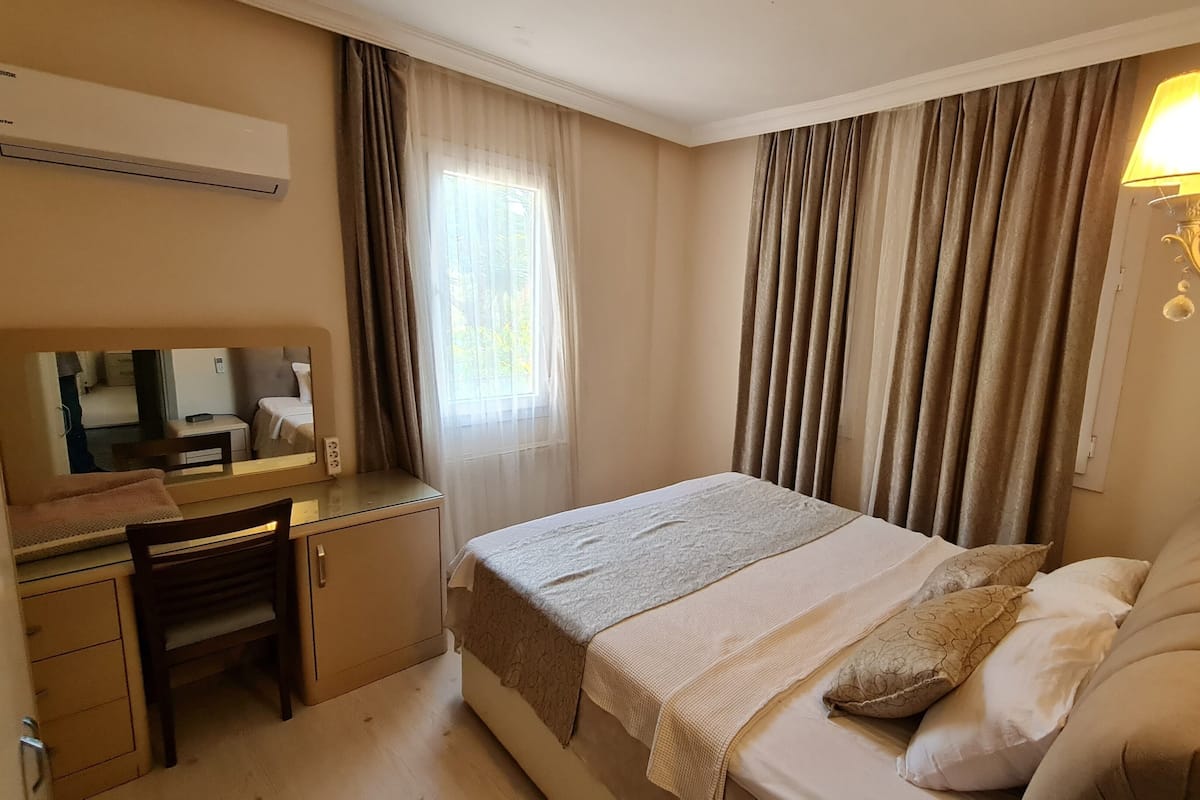 A hotel room with a bed, desk, chair, and a lamp.