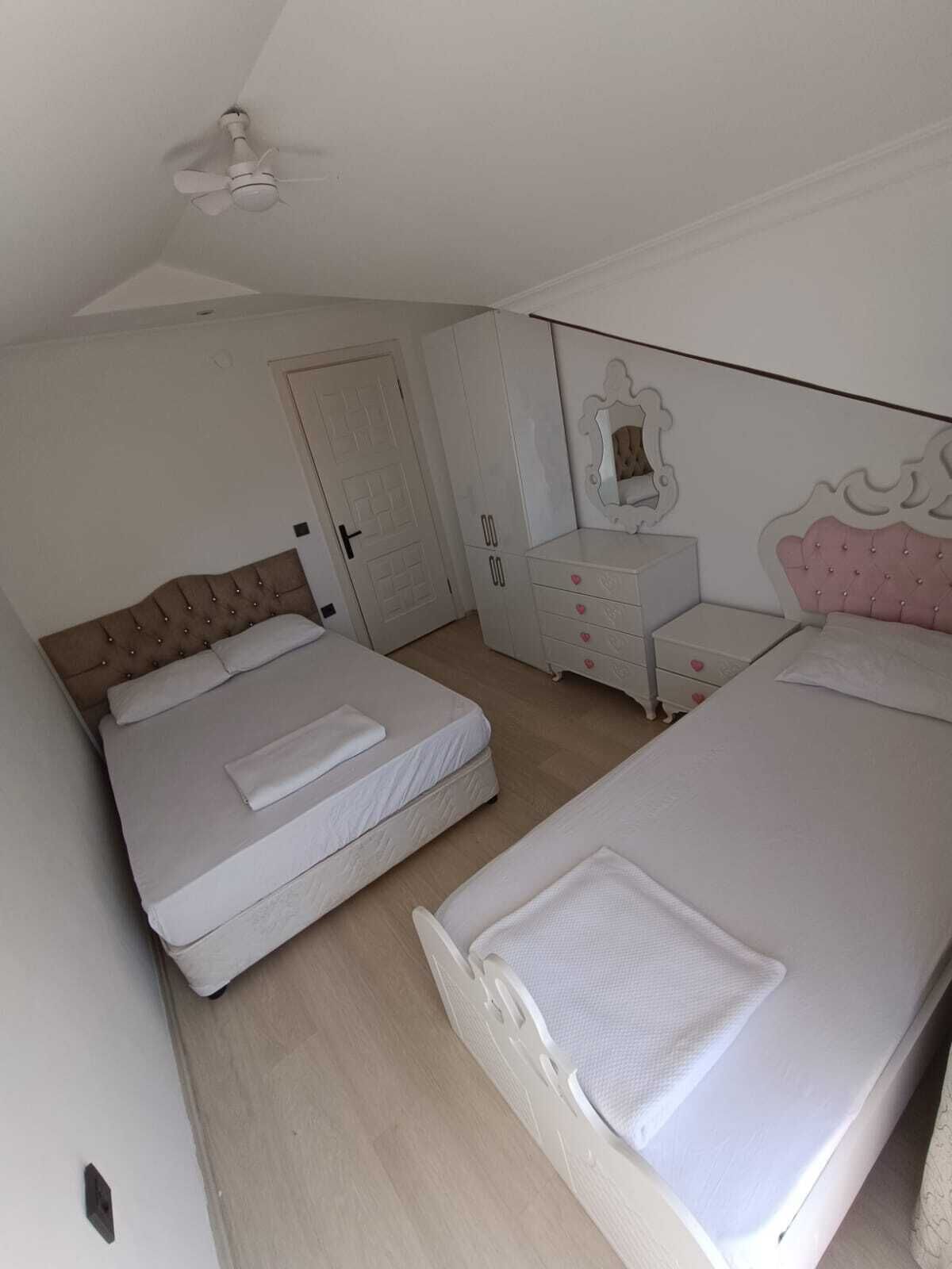 Une chambre avec deux lits, une commode, un miroir et un ventilateur de plafond.