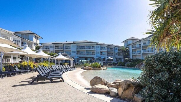 Um resort com piscina, espreguiçadeiras e um edifício com várias varandas.