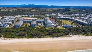 Resort costeiro com vários edifícios, uma praia de areia e ondas do oceano.