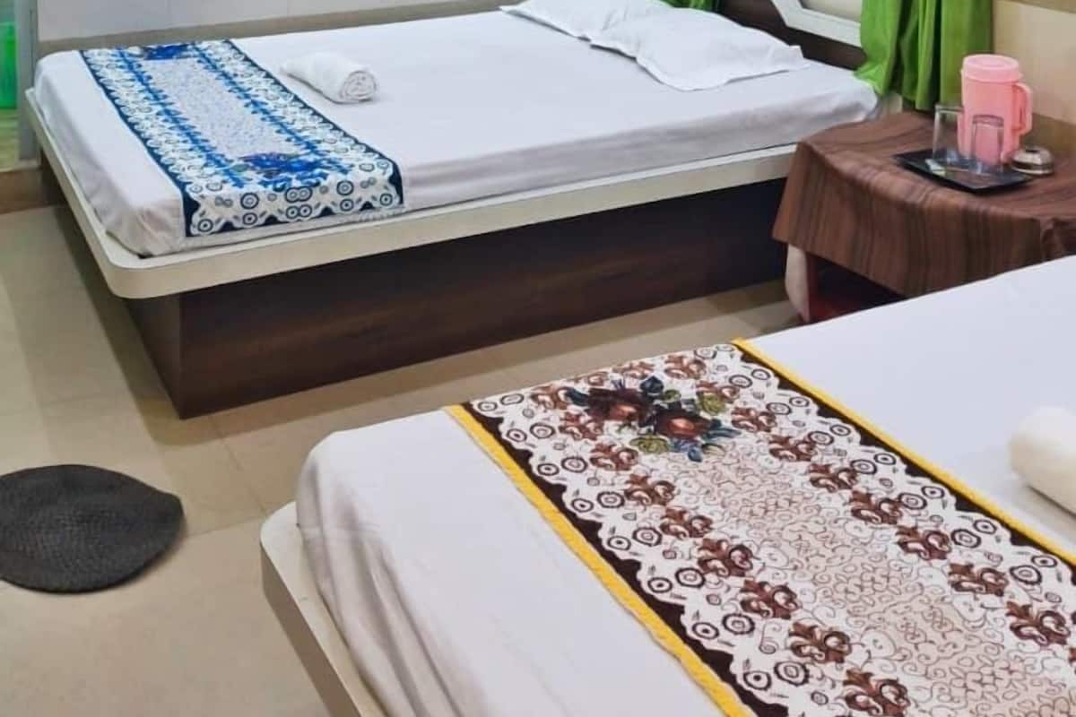 Habitación de hotel con dos camas, ventilador de techo, un tapiz decorativo y una ventana con cortinas.