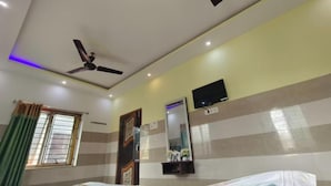 Une chambre d’hôtel avec un lit, un ventilateur de plafond, une télévision et une fenêtre avec des rideaux.
