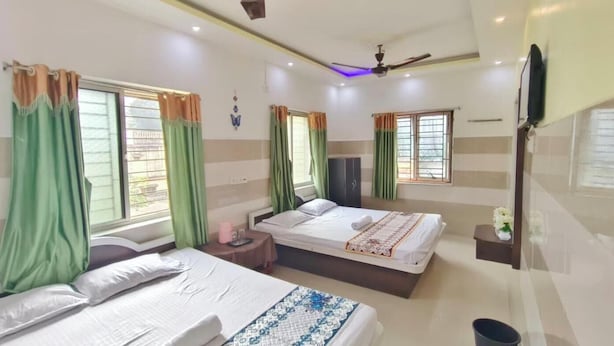 Une chambre d’hôtel avec deux lits, un ventilateur de plafond, un téléviseur à écran plat et une fenêtre avec des rideaux.