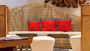 A modern hotel room with a rattan headboard, white sofa, and red cushions. There are wooden side tables and a patterned rug on the floor. - APEC TUY HOA   - PHU YEN CONDOTEL (Tuy Hoa)