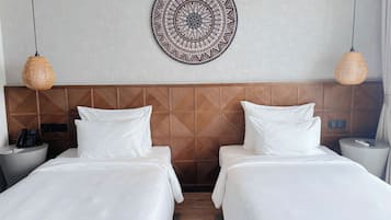 A hotel room with two beds, a patterned wall hanging, and two wicker lamps.