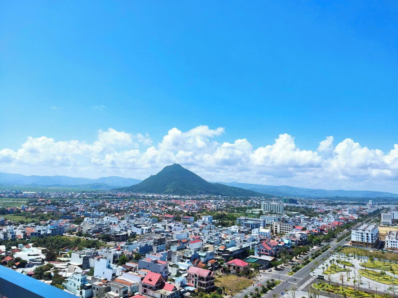 Una vista panorámica de una ciudad con una montaña destacada al fondo, numerosos edificios y un cielo despejado.