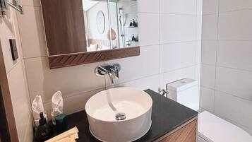 A modern bathroom with a large mirror, a round sink, and a toilet.