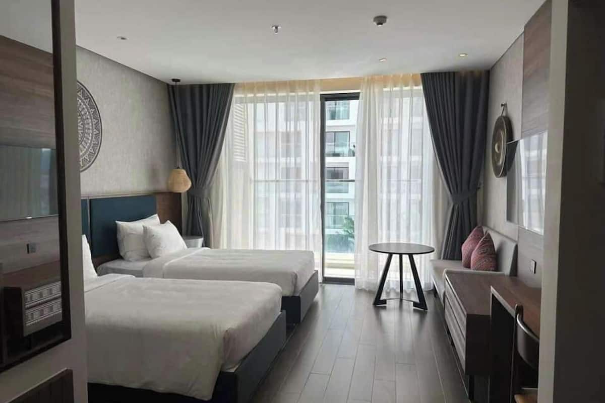 A hotel room with two beds, a small table, a TV, and a window with curtains.